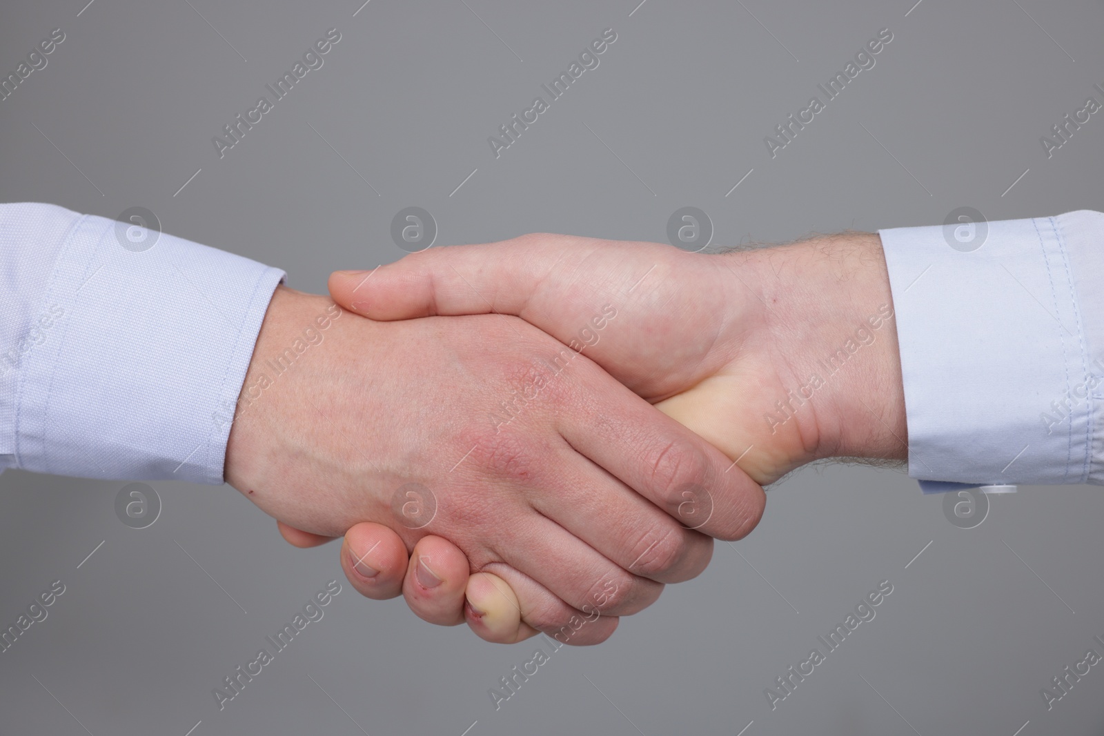 Photo of Businessmen shaking hands on grey background, closeup