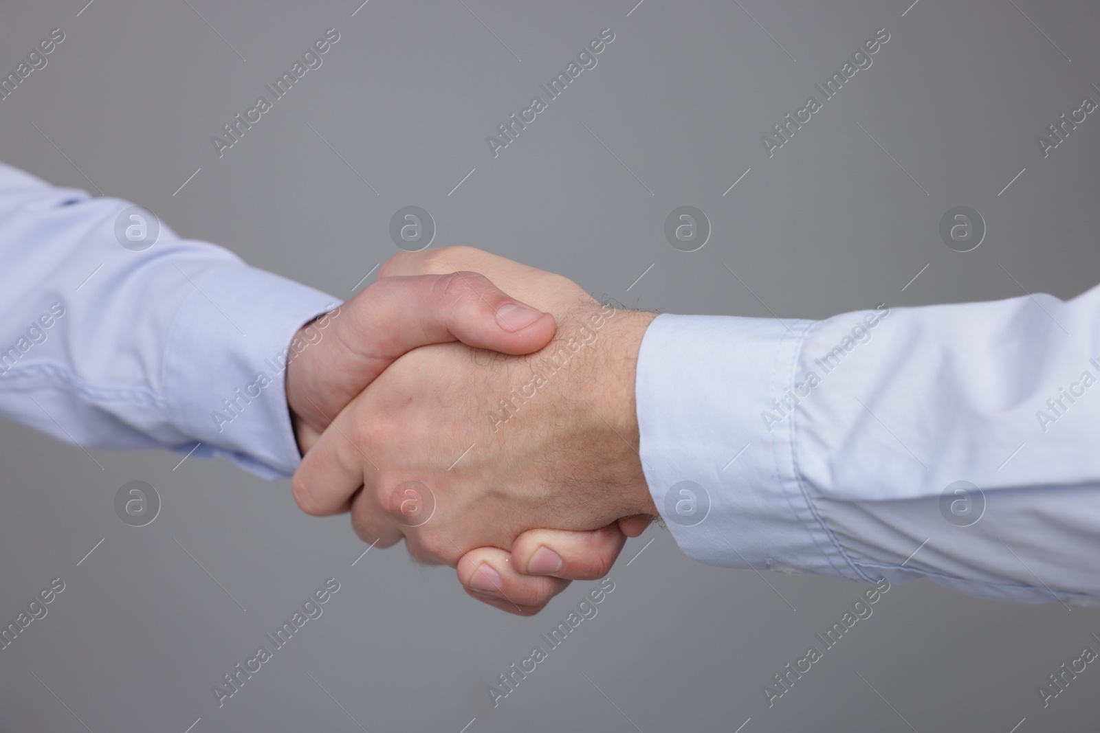 Photo of Businessmen shaking hands on grey background, closeup