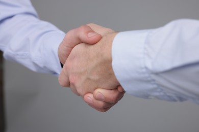 Photo of Businessmen shaking hands on grey background, closeup