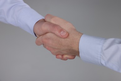 Photo of Businessmen shaking hands on grey background, closeup