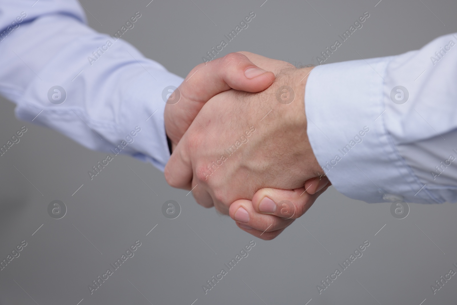 Photo of Businessmen shaking hands on grey background, closeup