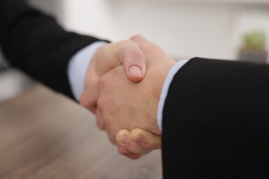 Photo of Businessmen shaking hands at wooden desk in office, closeup