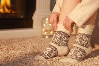 Photo of Woman in warm socks resting near fireplace at home, closeup. Space for text