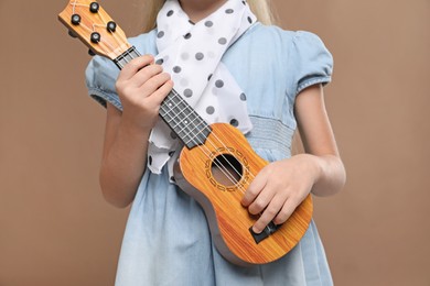 Photo of Little girl with ukulele on brown background, closeup