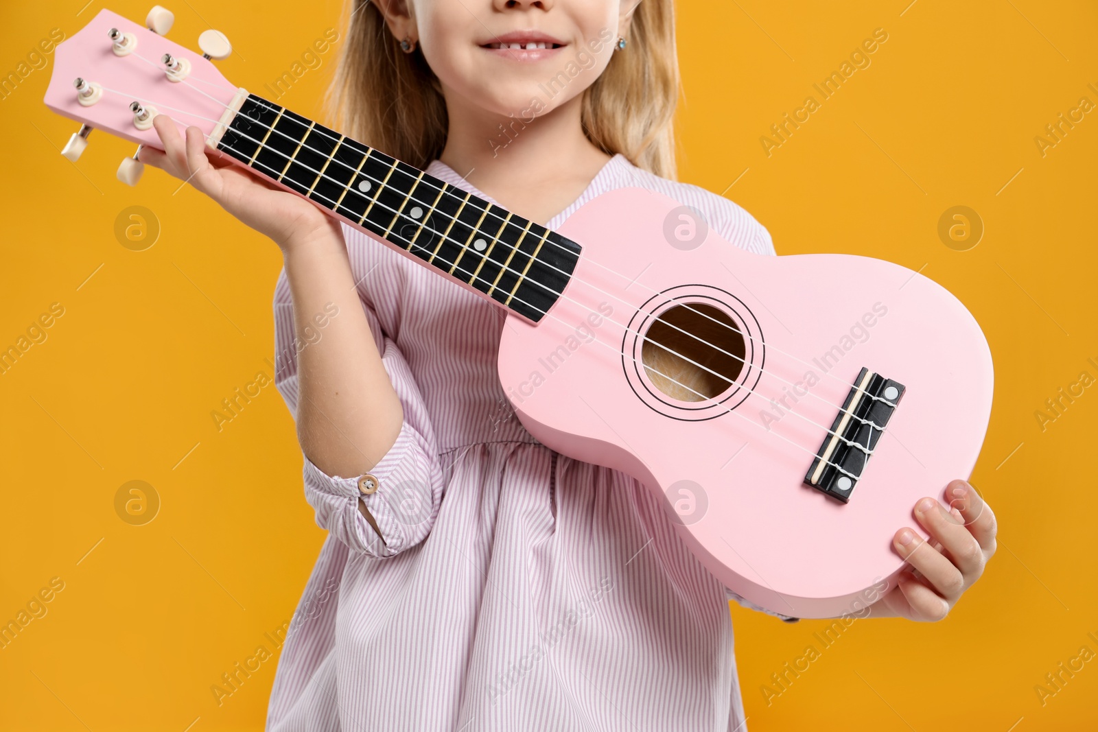 Photo of Little girl with ukulele on orange background, closeup