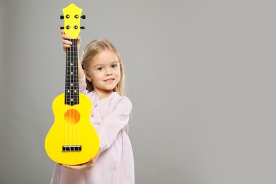 Photo of Little girl with ukulele on gray background, space for text