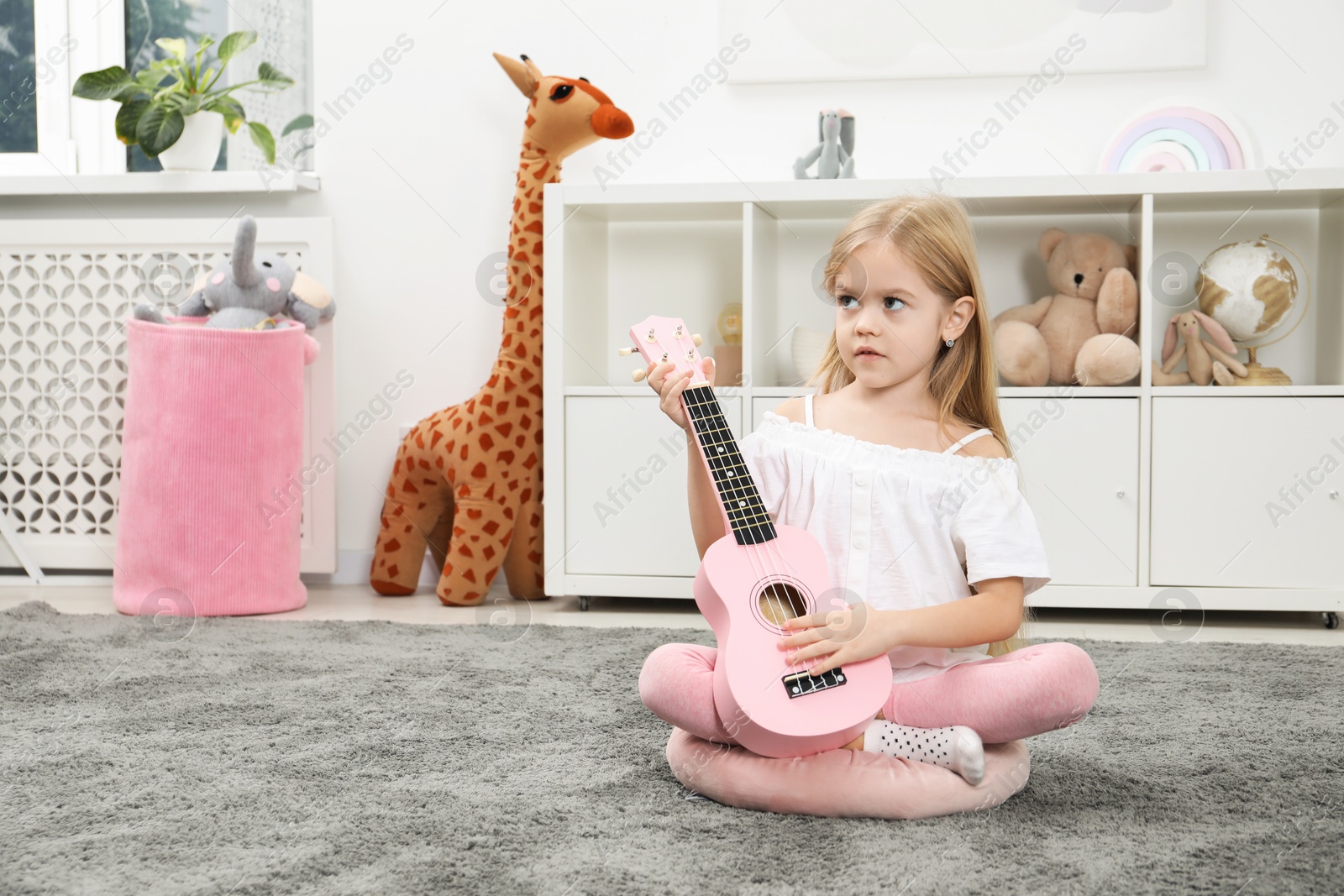 Photo of Cute little girl playing ukulele at home