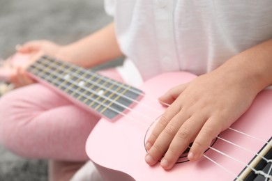 Photo of Little girl playing ukulele at home, closeup