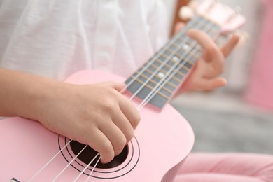 Photo of Little girl playing ukulele at home, closeup