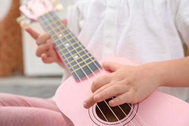 Photo of Little girl playing ukulele at home, closeup