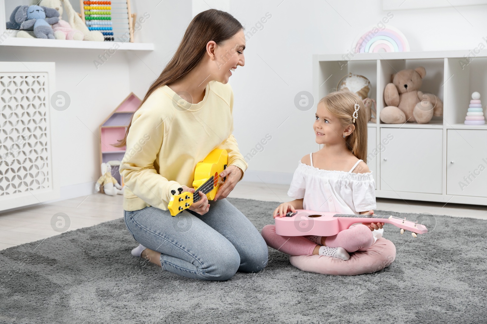 Photo of Young woman teaching little girl to play ukulele at home