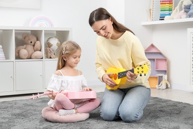 Photo of Young woman teaching little girl to play ukulele at home