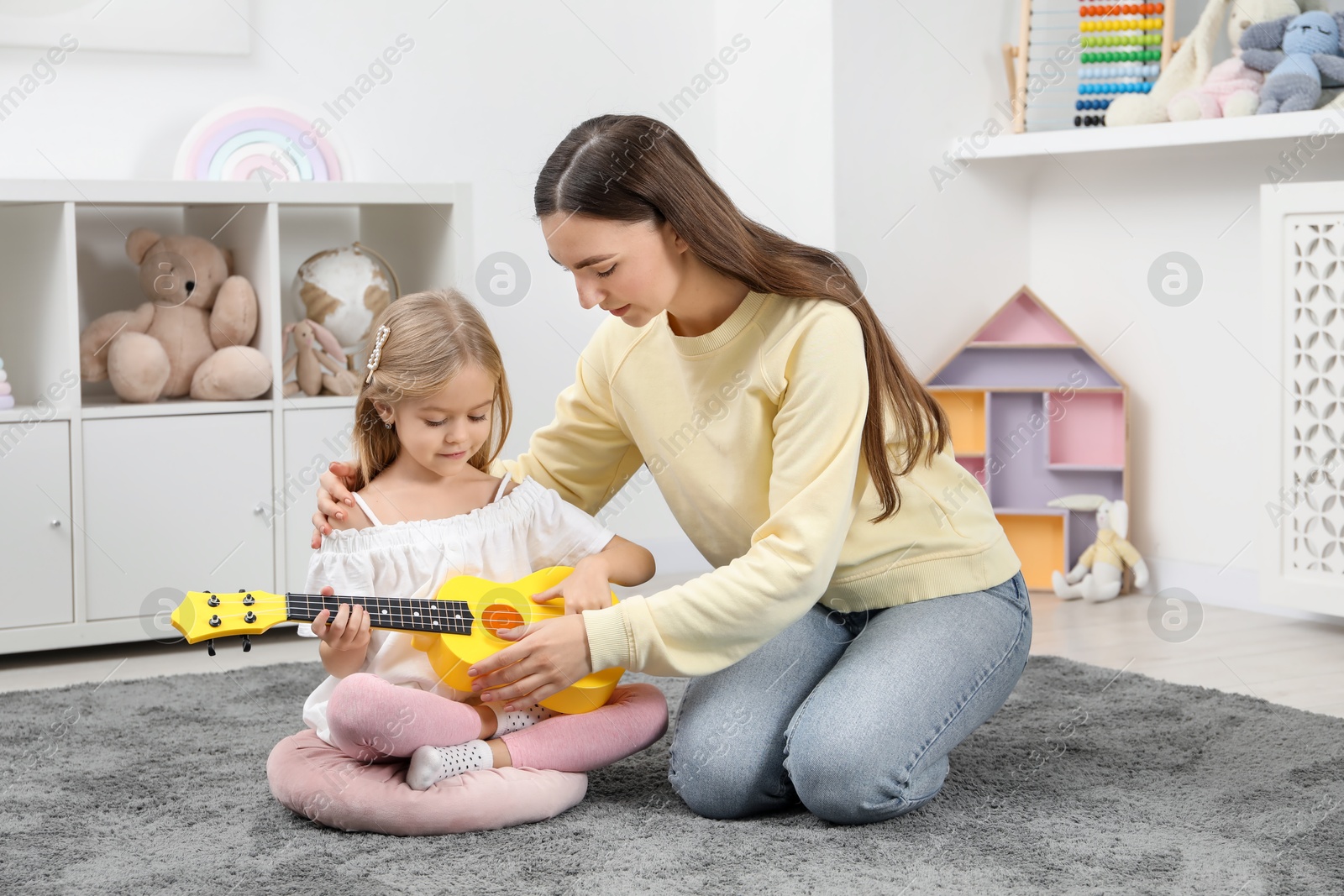 Photo of Young woman teaching little girl to play ukulele at home