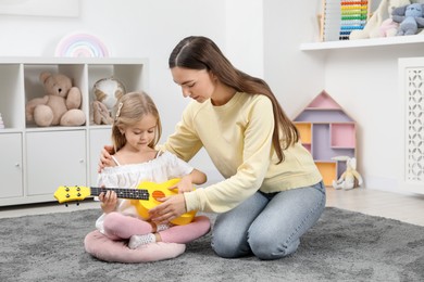 Young woman teaching little girl to play ukulele at home