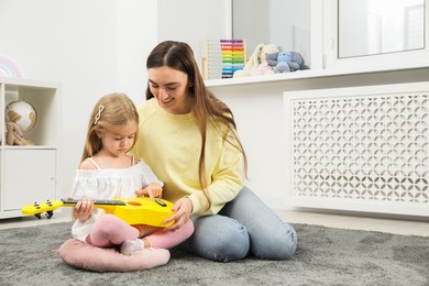 Young woman teaching little girl to play ukulele at home