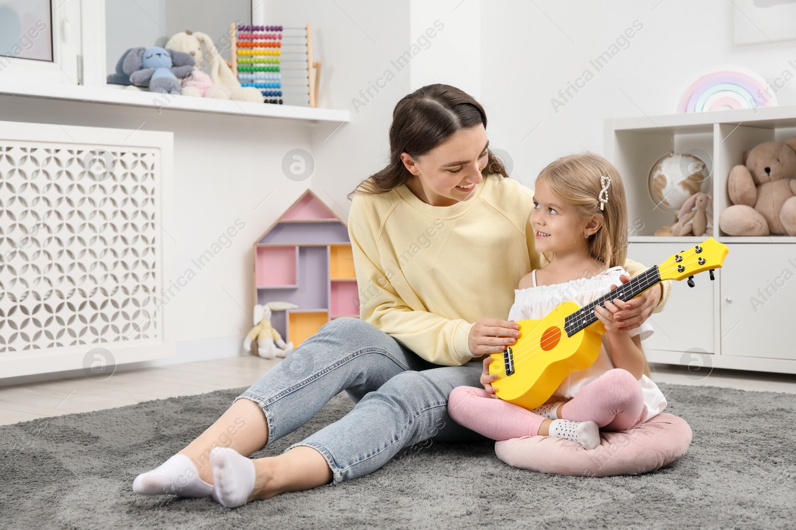 Photo of Young woman teaching little girl to play ukulele at home