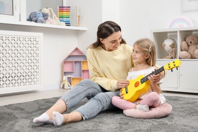 Photo of Young woman teaching little girl to play ukulele at home