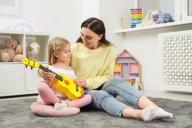 Young woman teaching little girl to play ukulele at home