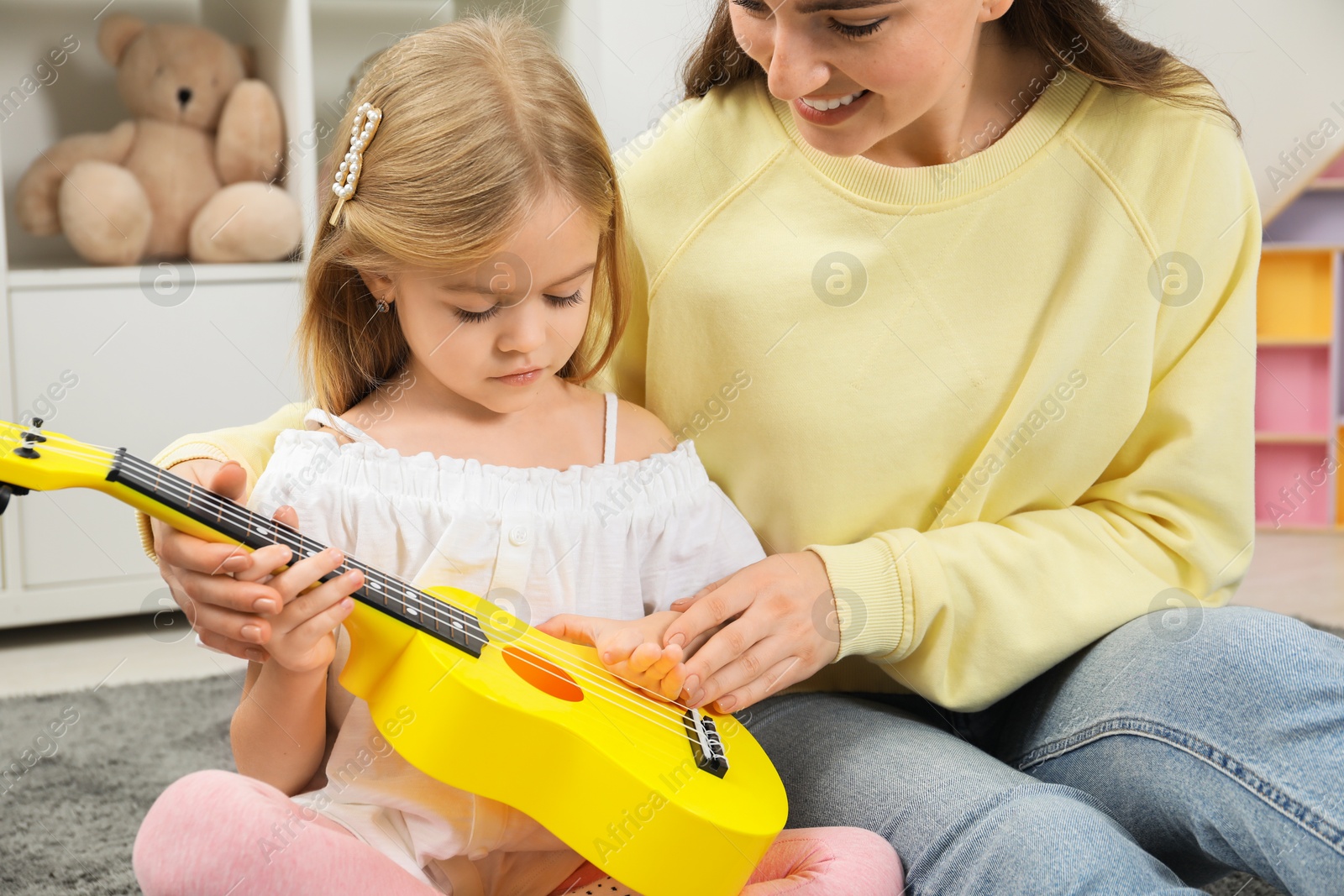 Photo of Young woman teaching little girl to play ukulele at home