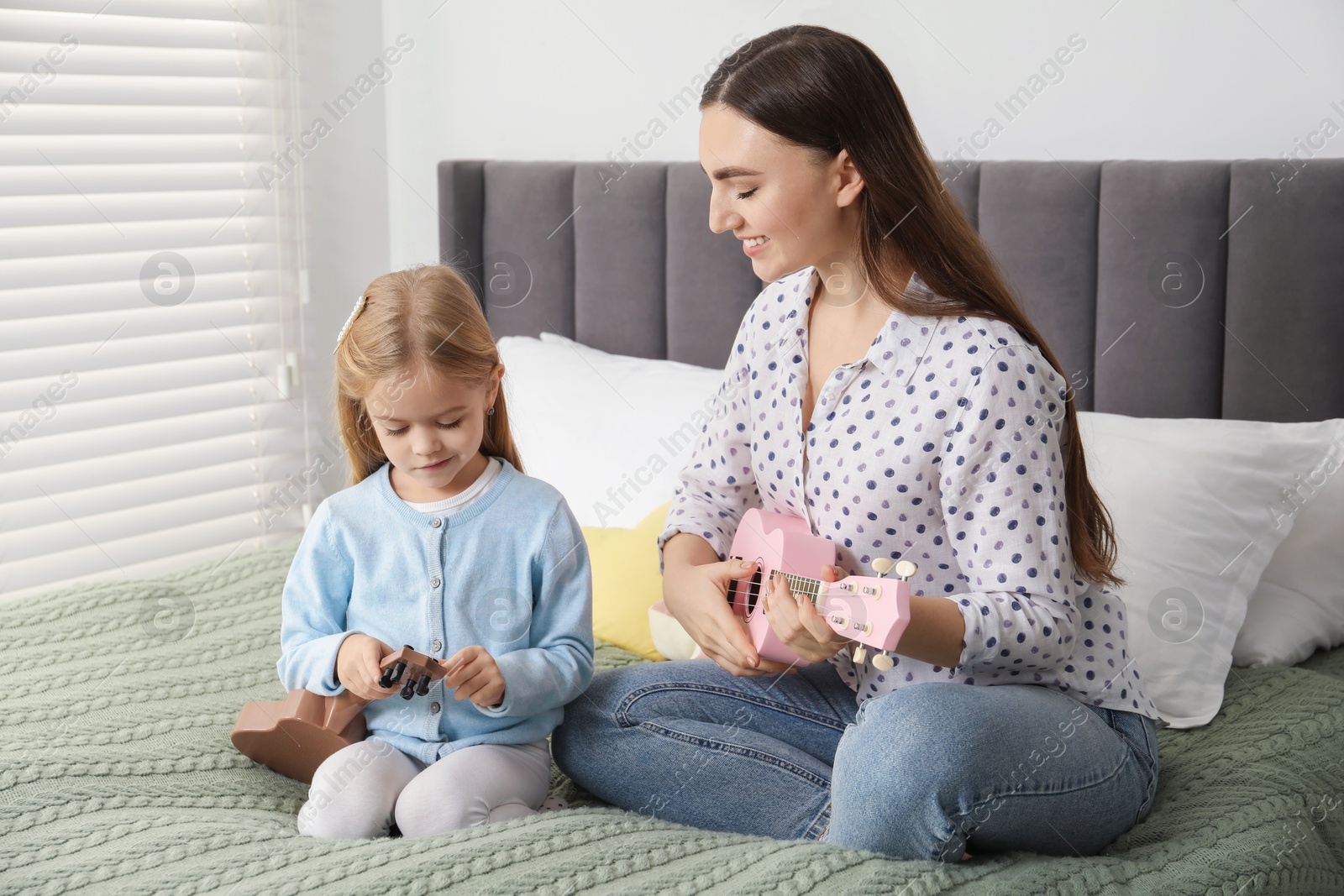 Photo of Young woman teaching little girl to play ukulele at home