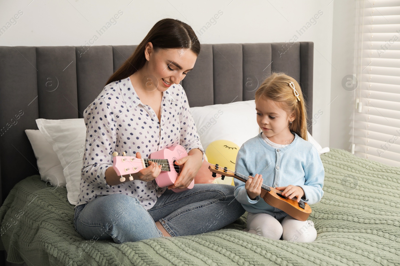 Photo of Young woman teaching little girl to play ukulele at home