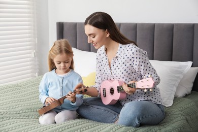 Young woman teaching little girl to play ukulele at home