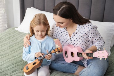 Photo of Young woman teaching little girl to play ukulele at home