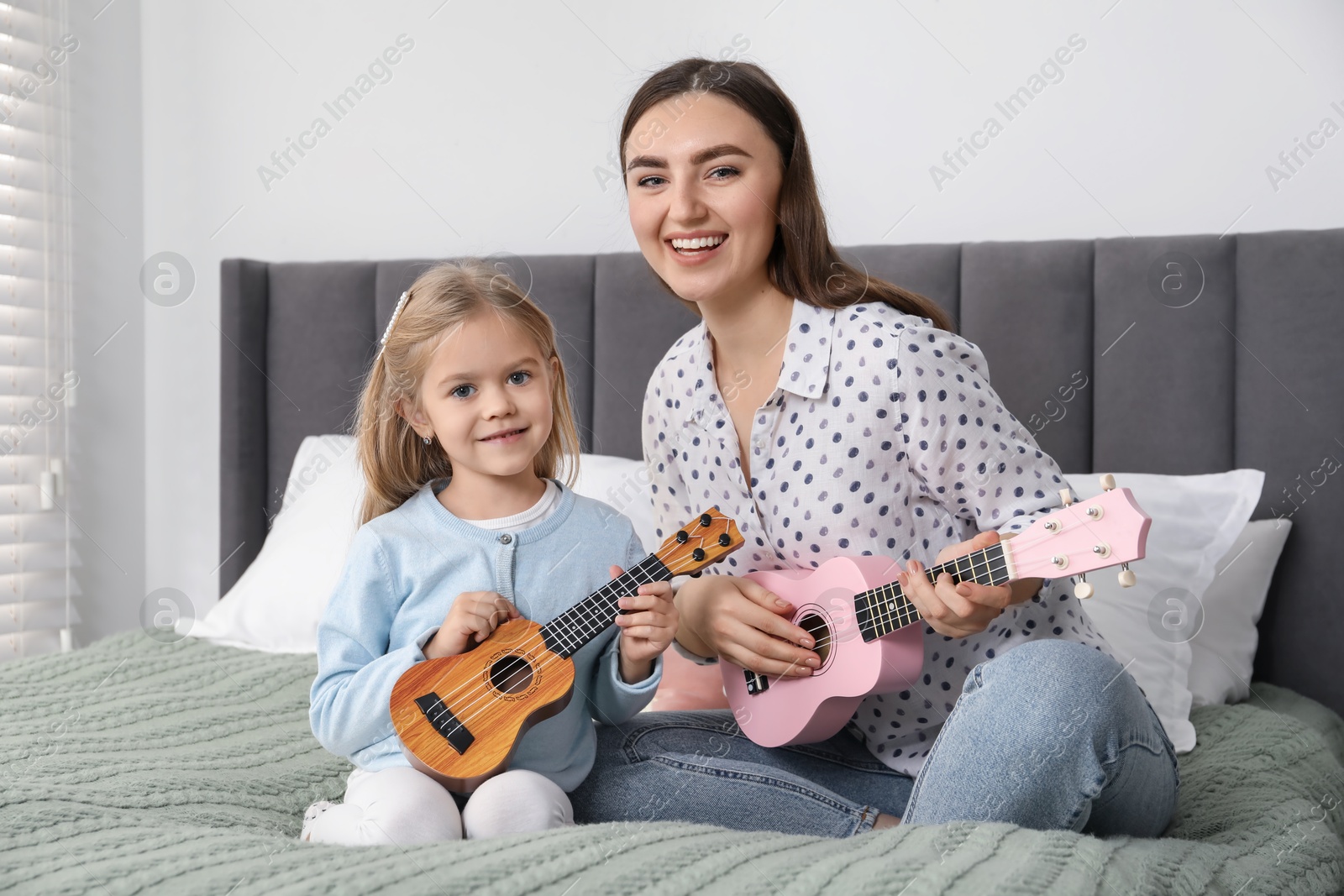 Photo of Young woman teaching little girl to play ukulele at home