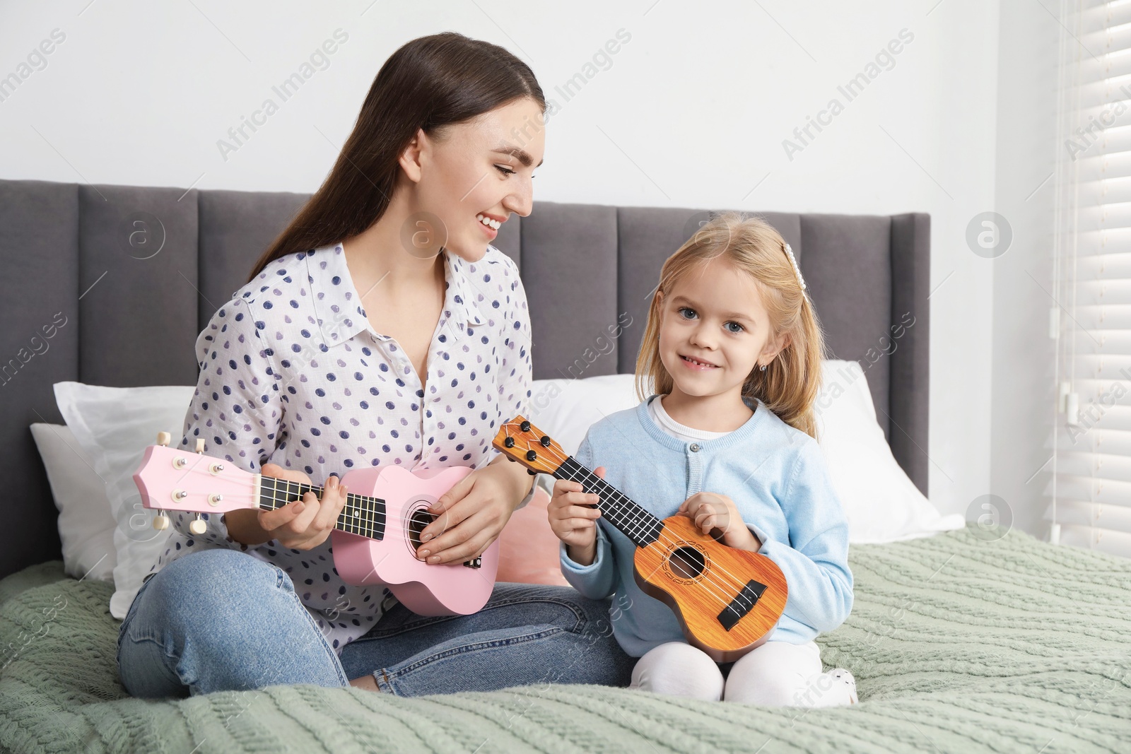 Photo of Young woman teaching little girl to play ukulele at home