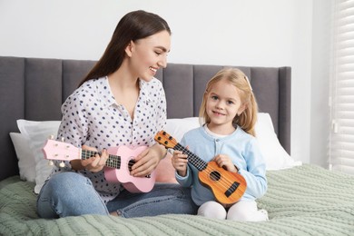 Young woman teaching little girl to play ukulele at home