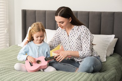 Photo of Young woman teaching little girl to play ukulele at home