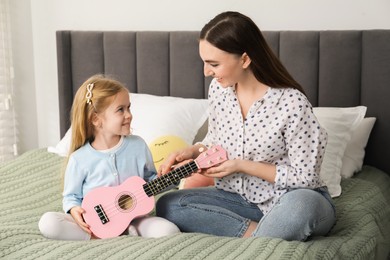 Photo of Young woman teaching little girl to play ukulele at home