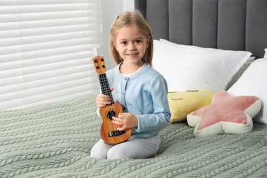 Photo of Little girl with ukulele on bed at home