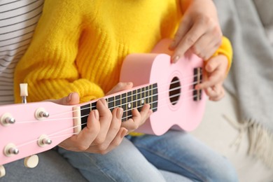 Photo of Woman teaching little girl to play ukulele at home, closeup