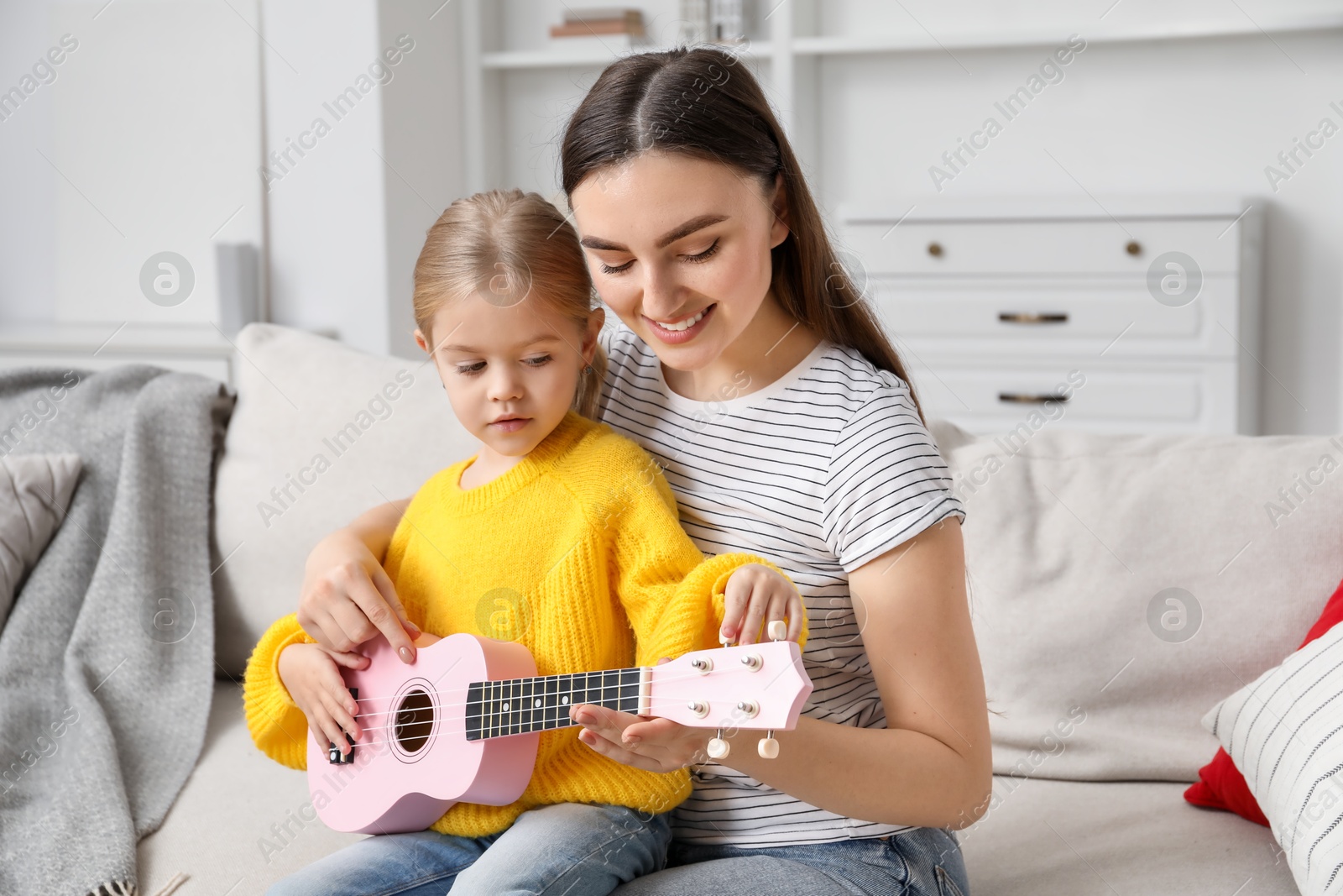 Photo of Young woman teaching little girl to play ukulele at home