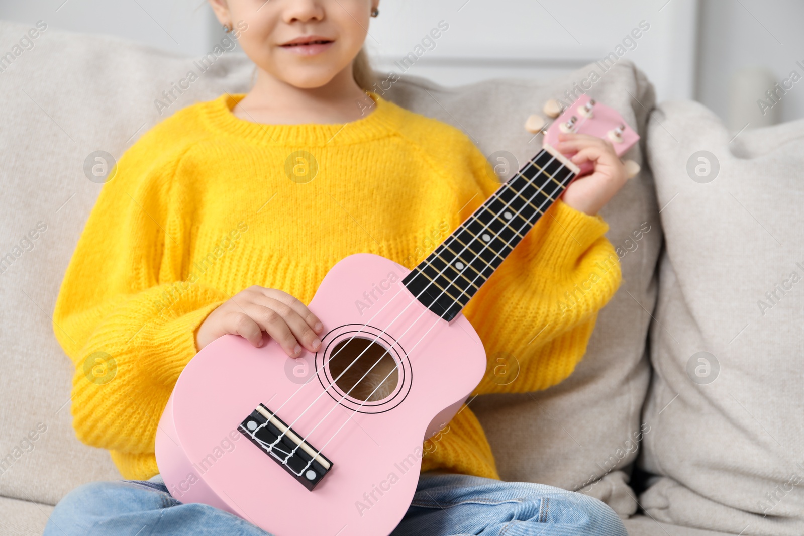 Photo of Little girl with ukulele on sofa at home, closeup