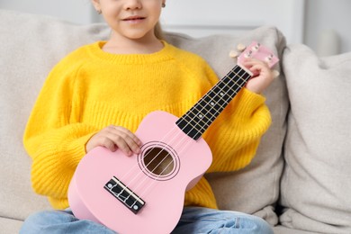 Photo of Little girl with ukulele on sofa at home, closeup