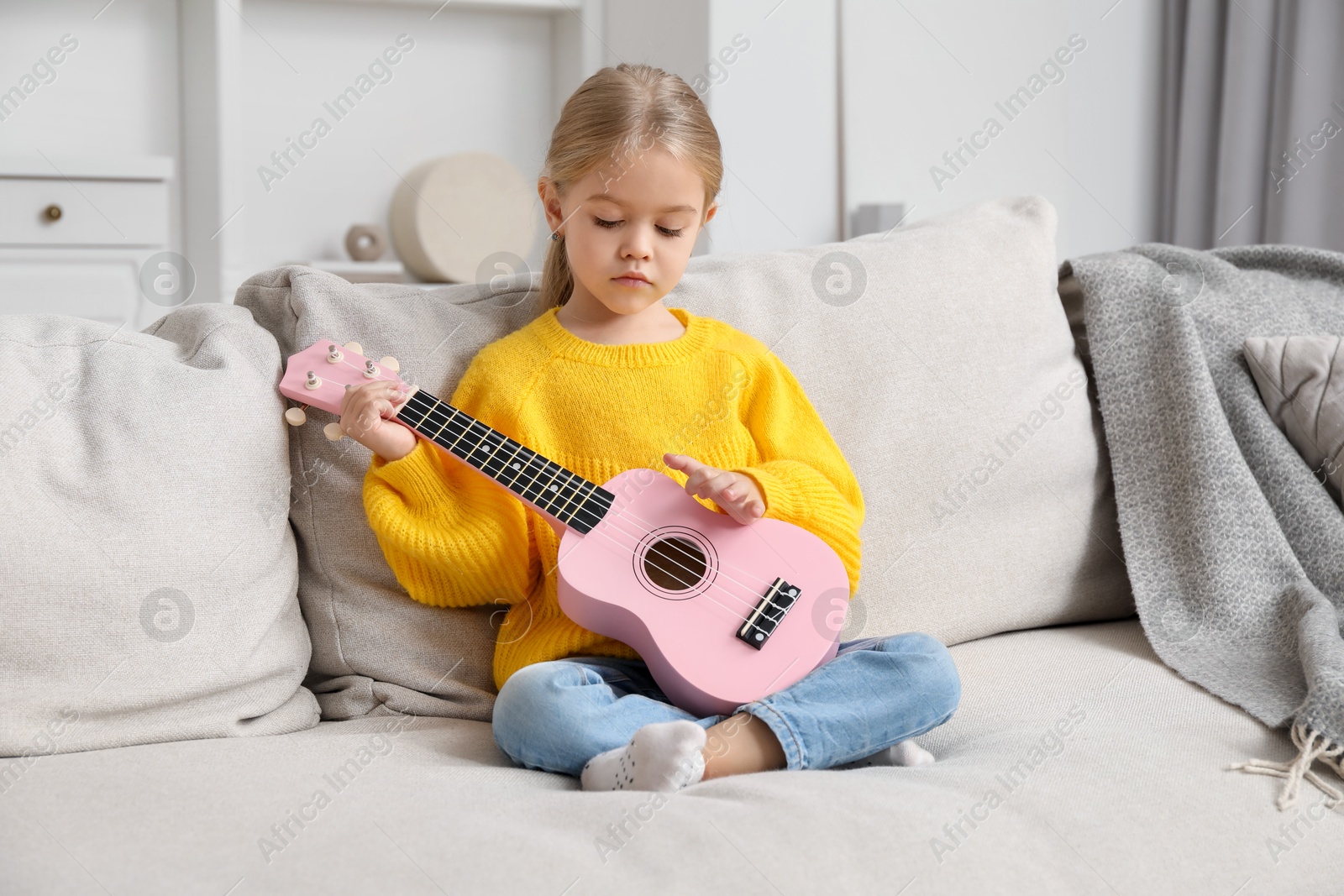 Photo of Little girl playing ukulele on sofa at home