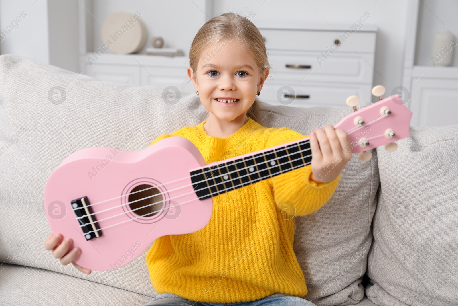 Photo of Little girl with ukulele on sofa at home