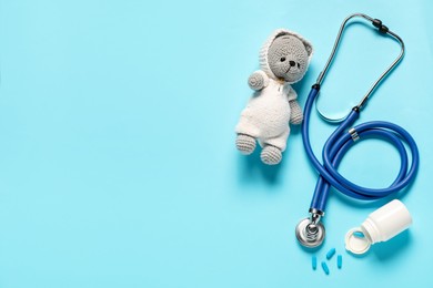 Photo of Pediatrics concept. Toy bear with stethoscope and pills on light blue background, flat lay. Space for text