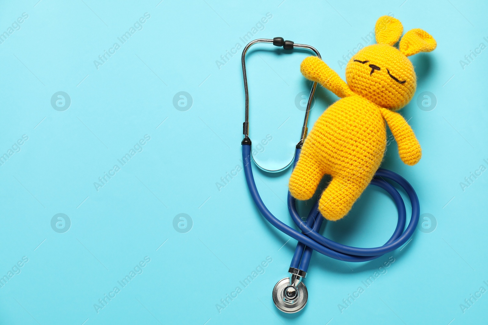 Photo of Pediatrics concept. Toy bunny with stethoscope on light blue background, top view. Space for text