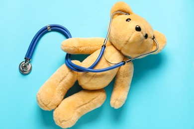 Photo of Pediatrics concept. Teddy bear with stethoscope on light blue background, top view