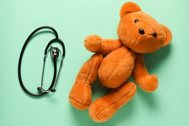 Photo of Pediatrics concept. Teddy bear with stethoscope on turquoise background, top view