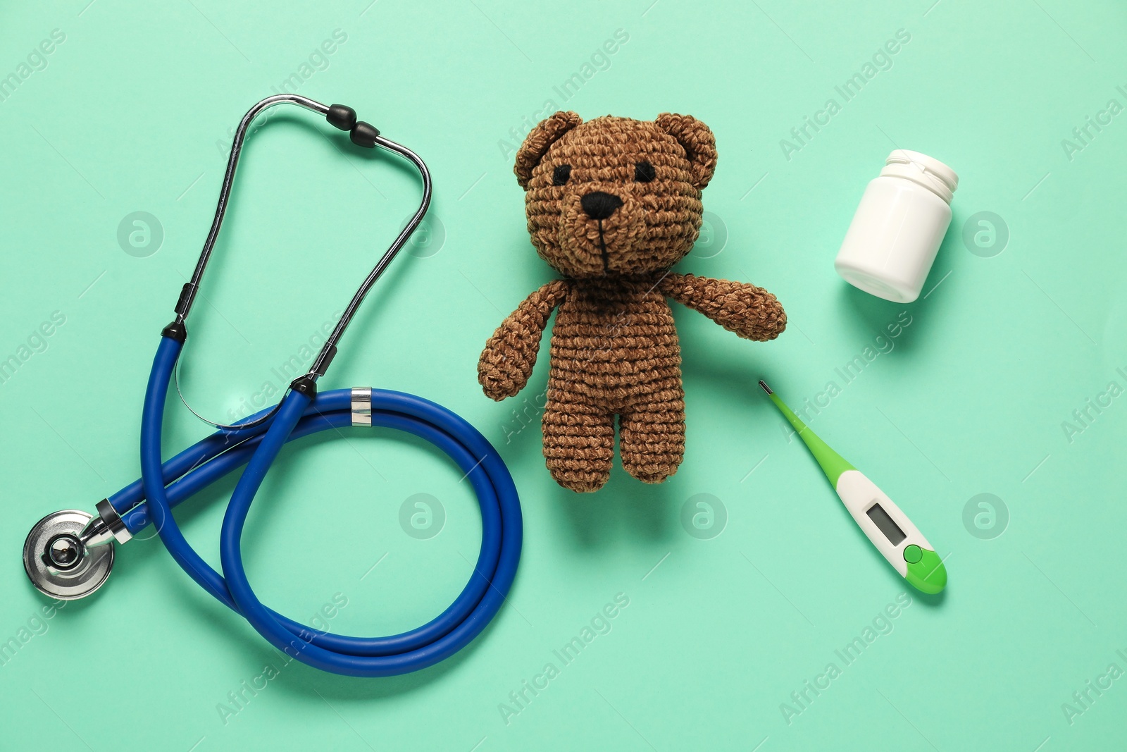 Photo of Pediatrics concept. Toy bear with stethoscope, pills and thermometer on turquoise background, flat lay