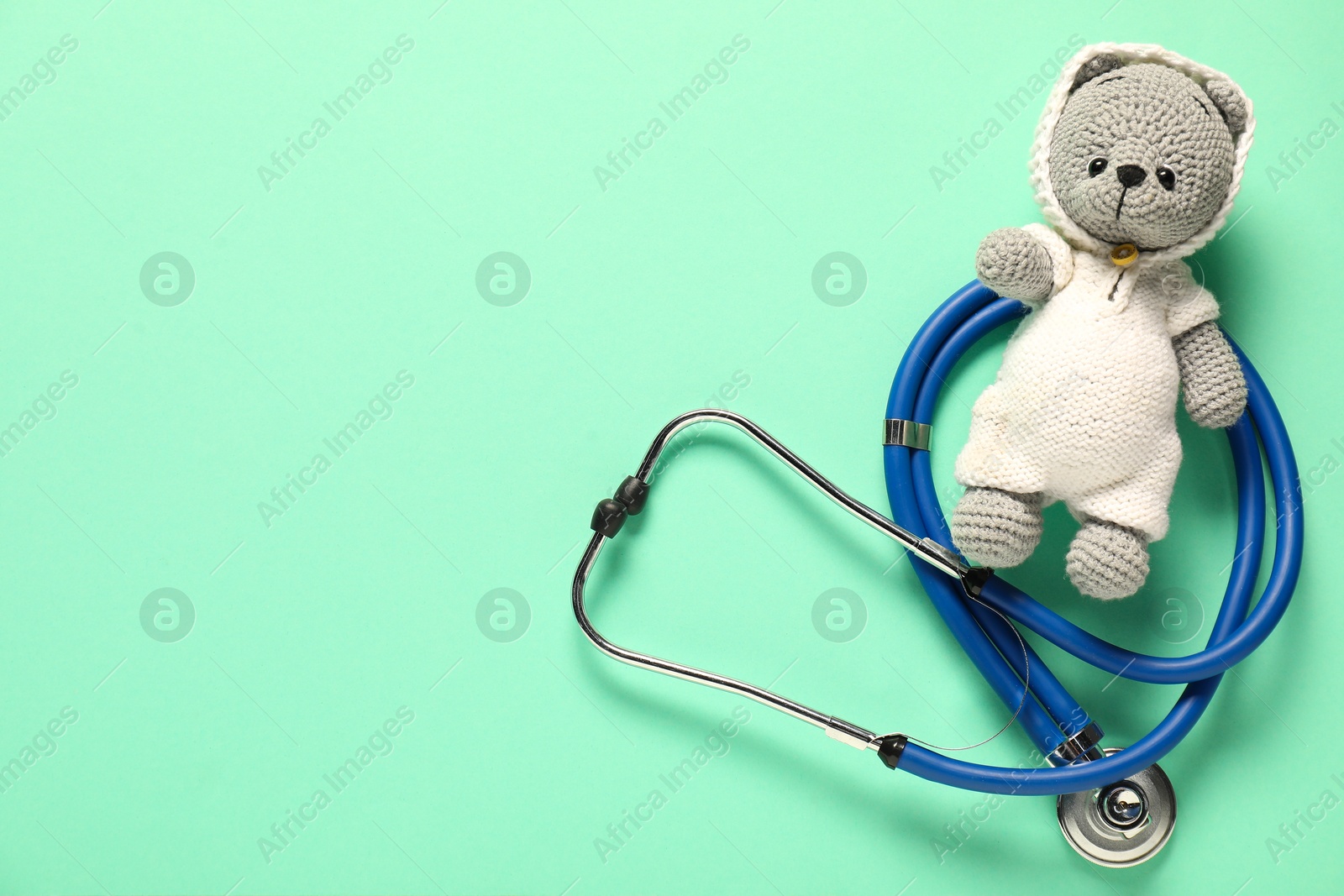 Photo of Pediatrics concept. Toy bear with stethoscope on turquoise background, top view. Space for text