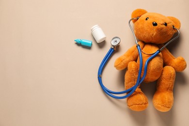 Photo of Pediatrics concept. Teddy bear with stethoscope, nasal spray and pills on beige background, flat lay. Space for text