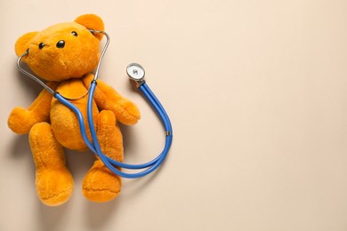 Photo of Pediatrics concept. Teddy bear with stethoscope on beige background, top view. Space for text