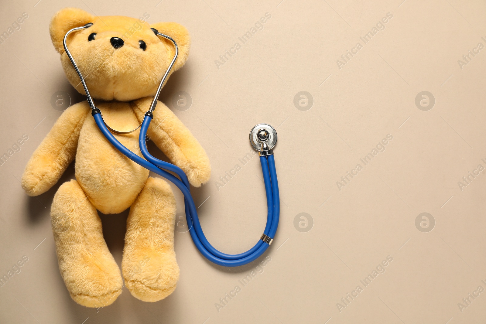 Photo of Pediatrics concept. Teddy bear with stethoscope on beige background, top view. Space for text