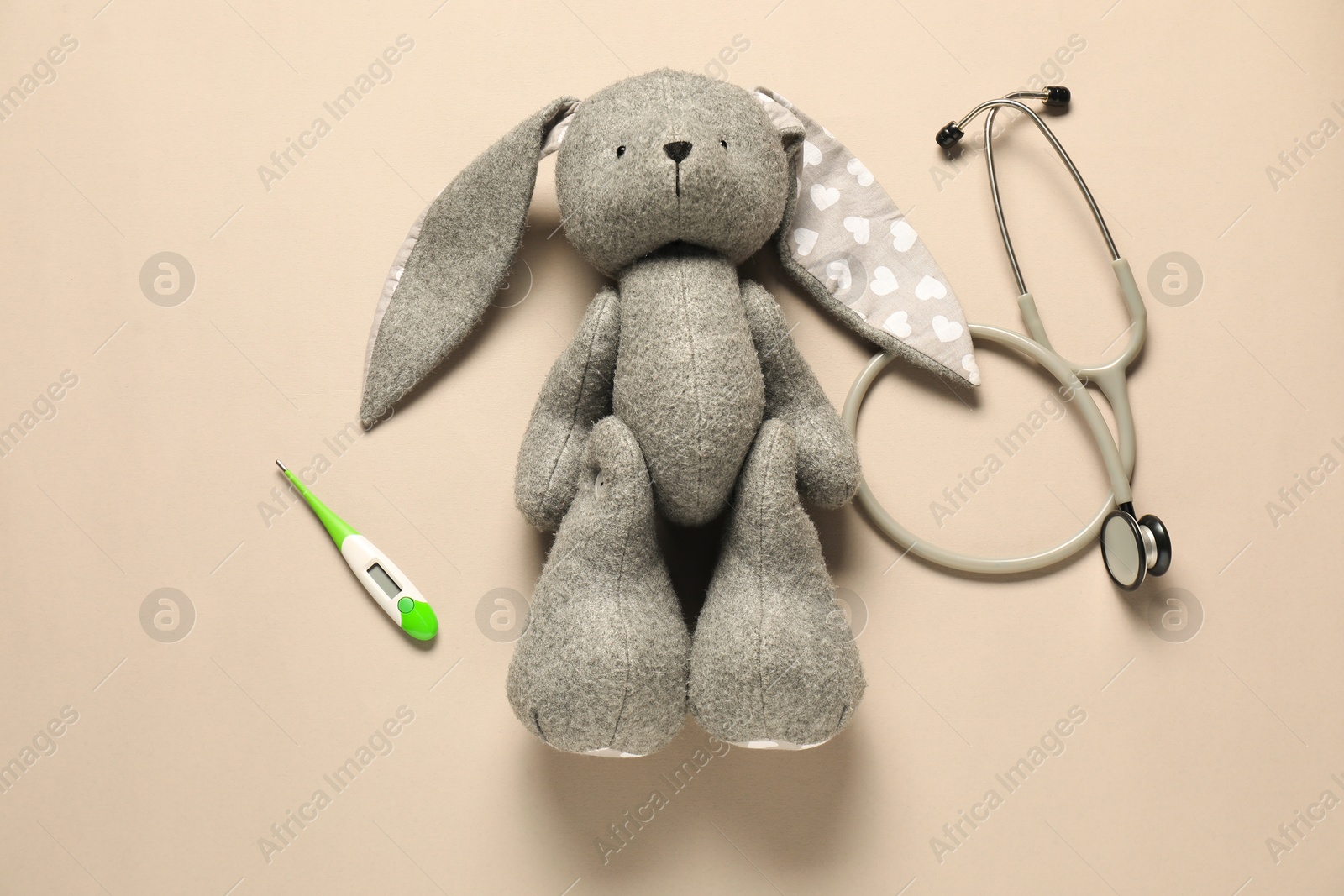 Photo of Pediatrics concept. Toy bunny with stethoscope and thermometer on beige background, flat lay