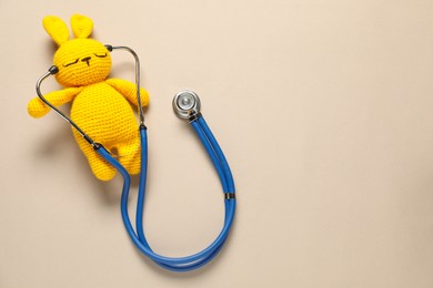 Photo of Pediatrics concept. Toy bunny with stethoscope on beige background, top view. Space for text